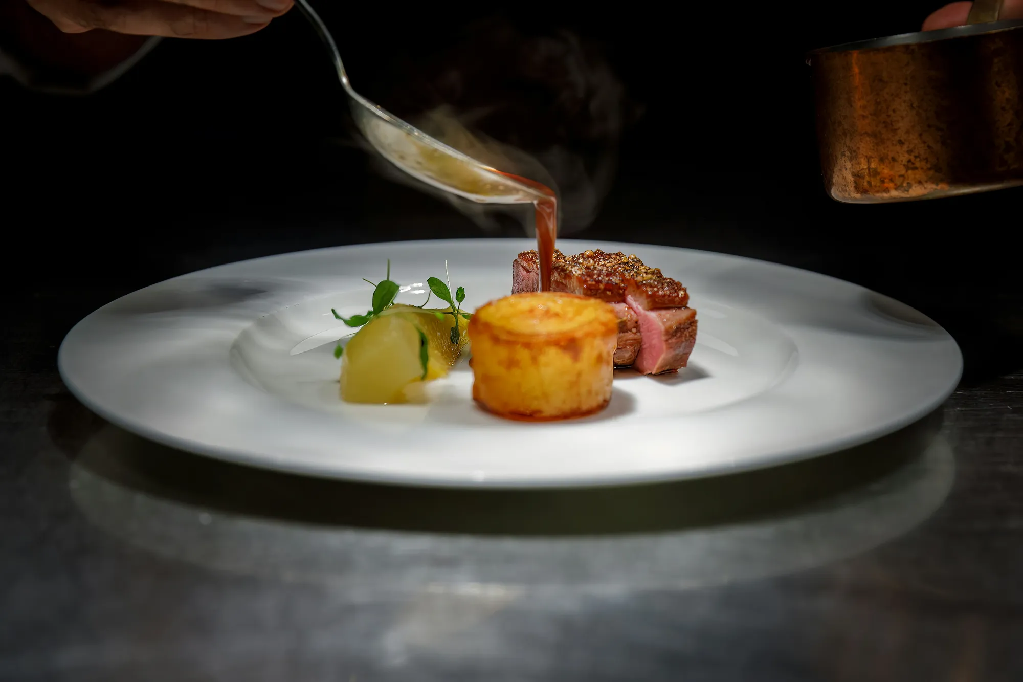 A chef finishing a plated dish with sauce